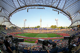 Interior view of Munich Olympic Stadium during the 2022 European Athletics Championships. The red synthetic running track and central field are ready for competition, with broadcast cameras and spectators capturing the live atmosphere.